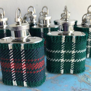 Op de afbeelding: Een verzameling kleine roestvrijstalen heupflacons met zilveren schroefdoppen. Elke flacon is omwikkeld met een groen, marineblauw, rood en wit geruit patroon. De flacons hebben een kleine lus aan de bovenkant.