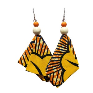Peut inclure: Paire de boucles d'oreilles faites à la main avec un motif géométrique jaune, orange et noir. Chaque boucle d'oreille est ornée d'une perle en bois et d'une petite perle orange, suspendues à un crochet argenté.