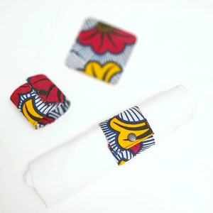Peut inclure: Une serviette blanche roulée avec un anneau de serviette à motifs et deux dessous de verre assortis. L'anneau de serviette et les dessous de verre présentent un motif floral coloré avec des accents rouges, jaunes et bleus. Les dessous de verre sont carrés.