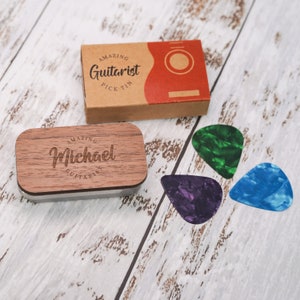 May include: A wooden box with the text "Amazing Guitarist" and the name "Michael" engraved on it. The box is open and contains three guitar picks in green, blue, and purple.