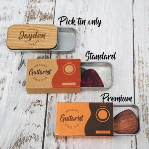 May include: Three guitar pick tins with different options. The first tin is a wooden box with the name "Jayden" engraved on it. The second tin is a brown cardboard box with the words "Amazing Guitarist Pick Tin" printed on it. The third tin is a brown cardboard box with the words "Amazing Guitarist Pick Tin" printed on it. The second and third tins have a guitar pick inside.