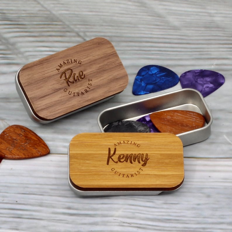May include: Two small wooden boxes with metal lids. The lids are engraved with the words "Amazing Rae Guitarist" and "Amazing Kenny Guitarist". The boxes are filled with guitar picks.