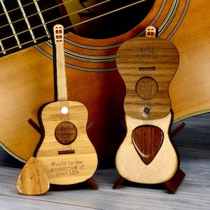 May include: Two miniature wooden acoustic guitars with a pick holder. One guitar has the text "Music is the soundtrack of your life" engraved on it. The other guitar has the text "Ellie's Pick" engraved on it.