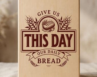 Puede incluir: Una tabla de cortar rectangular de madera clara con un grabado en color marrón oscuro. El texto dice GIVE US THIS DAY OUR DAILY BREAD, acompañado de ilustraciones de una hogaza de pan y espigas de trigo en un diseño decorativo.