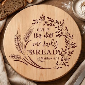 Könnte beinhalten: Ein rundes Holzschneidebrett mit der Gravur "GIVE US this day our daily BREAD Matthew 6:11", umgeben von Weizen- und Blumendesigns. Das Brett ist hellbraun und aus Holz gefertigt.