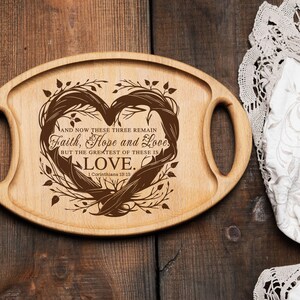 Puede incluir: Una bandeja de servir de madera con dos asas, que presenta un dise&ntilde;o en forma de coraz&oacute;n con un patr&oacute;n floral marr&oacute;n y el texto "AND NOW THESE THREE REMAIN Faith, Hope and Love. BUT THE GREATEST OF THESE IS LOVE. 1 Corinthians 13:13"