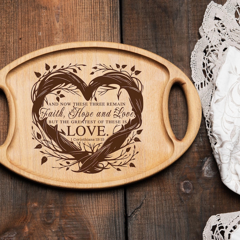 Puede incluir: Una bandeja de servir de madera con dos asas, que presenta un dise&ntilde;o en forma de coraz&oacute;n con un patr&oacute;n floral marr&oacute;n y el texto "AND NOW THESE THREE REMAIN Faith, Hope and Love. BUT THE GREATEST OF THESE IS LOVE. 1 Corinthians 13:13"