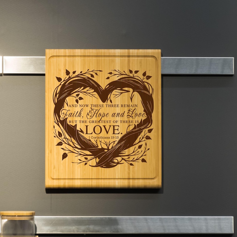 Puede incluir: Una tabla de cortar de madera con un dise&ntilde;o en forma de coraz&oacute;n y el texto "AND NOW THESE THREE REMAIN Faith, Hope and Love BUT THE GREATEST OF THESE IS LOVE. 1 Corinthians 13:13"