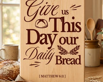 May include: A rectangular light-colored wooden cutting board featuring dark brown engraved text that reads Give us This Day our Daily Bread with a small bread loaf icon, wheat stalks, and the citation Matthew 6:11 at the bottom center.