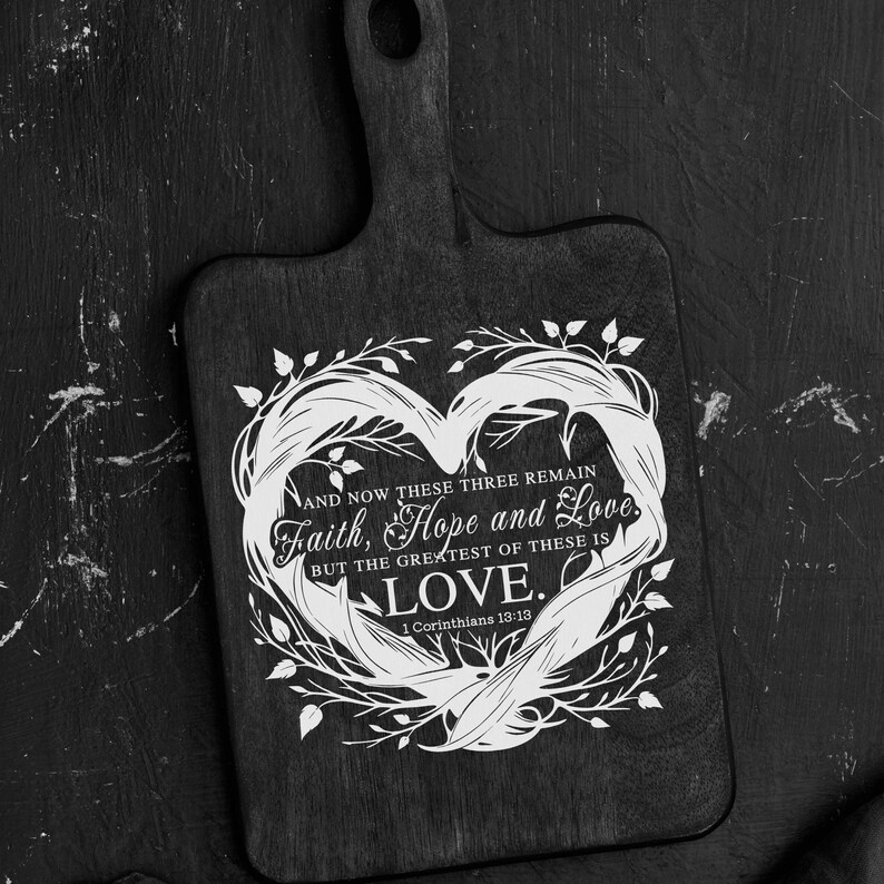 Puede incluir: Una tabla de cortar negra con un dise&ntilde;o de coraz&oacute;n blanco y el texto "AND NOW THESE THREE REMAIN Faith, Hope and Love. BUT THE GREATEST OF THESE IS LOVE. 1 Corinthians 13:13"