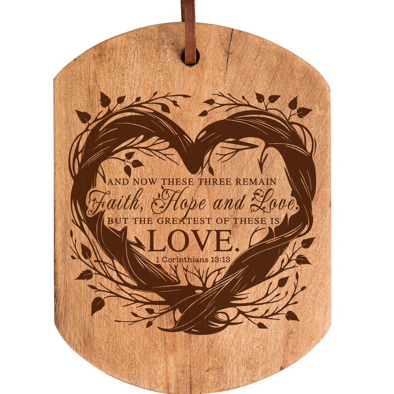 Puede incluir: Un letrero de madera en forma de coraz&oacute;n con un acabado de madera marr&oacute;n. El letrero presenta un dise&ntilde;o de rama de &aacute;rbol estilizado con el texto "AND NOW THESE THREE REMAIN Faith, Hope and Love BUT THE GREATEST OF THESE IS LOVE. 1 Corinthians 13:13".