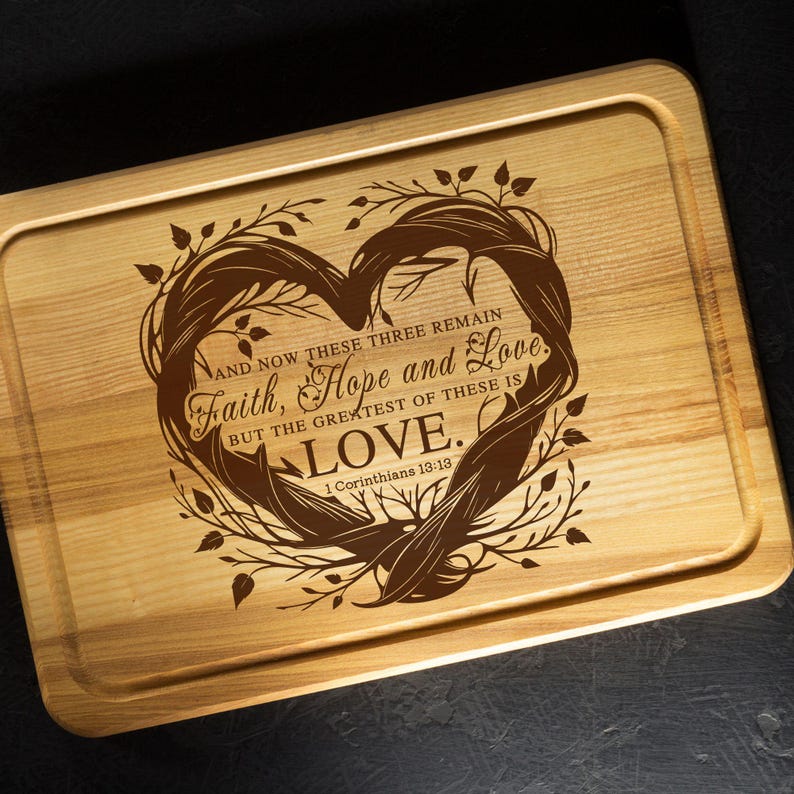Puede incluir: Tabla de cortar de madera con un dise&ntilde;o en forma de coraz&oacute;n y el texto "AND NOW THESE THREE REMAIN Faith, Hope and Love. BUT THE GREATEST OF THESE IS LOVE. 1 Corinthians 13:13"