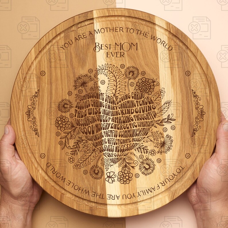 May include: A round wooden serving board with a heart-shaped design engraved with the words "You are a mother to the whole world. Best Mom Ever." and a list of positive adjectives. The board is made of light brown wood with a natural grain.