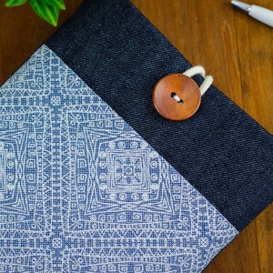 May include: A blue denim and white fabric pouch with a wooden button closure. The pouch has a geometric pattern on the front.