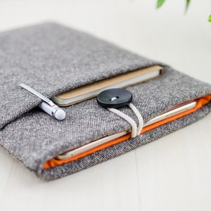 May include: A gray felt tablet sleeve with a brown notebook and a silver pen inside. The sleeve has a black button and a white string closure.