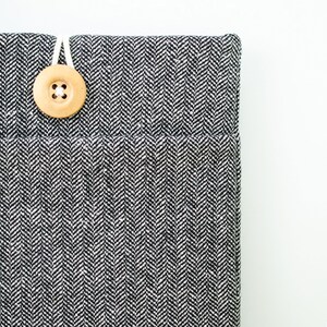 May include: A black and white herringbone fabric laptop sleeve with a wooden button closure.
