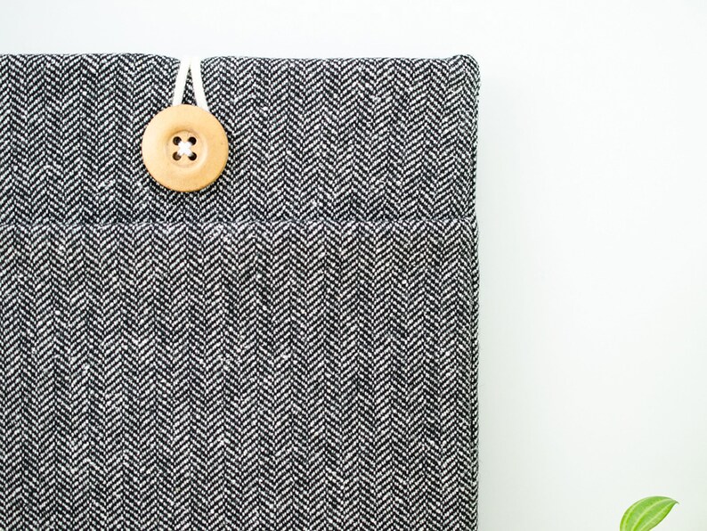 May include: A black and white herringbone fabric laptop sleeve with a wooden button closure.