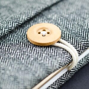 May include: A black and white herringbone fabric notebook with a wooden button closure and a white string tie.