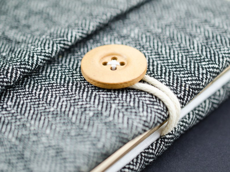 May include: A black and white herringbone fabric notebook with a wooden button closure and a white string tie.
