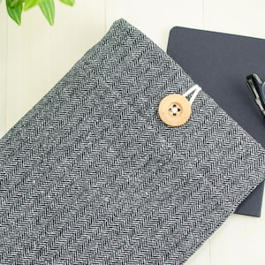 May include: A black and white herringbone fabric laptop sleeve with a wooden button closure.