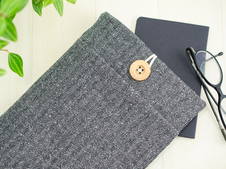 May include: A black and white herringbone fabric laptop sleeve with a wooden button closure.