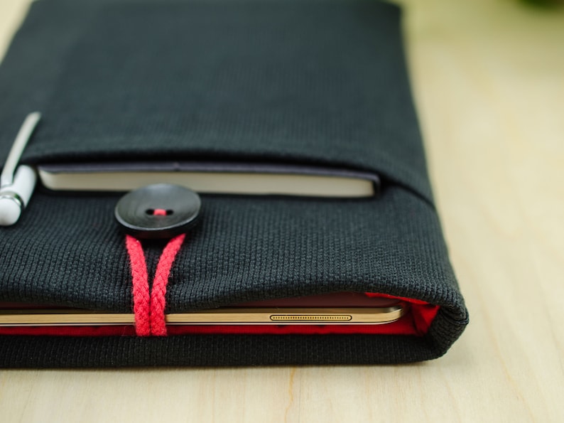 May include: A black canvas case with a red button and string closure. A tablet and pen are inside the case.