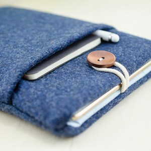 May include: A blue felt tablet sleeve with a brown button closure and a white cord. A notebook and a stylus are inside the sleeve.