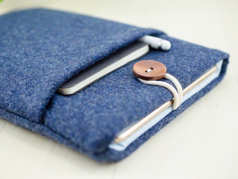 May include: A blue felt tablet sleeve with a brown button closure and a white cord. A notebook and a stylus are inside the sleeve.