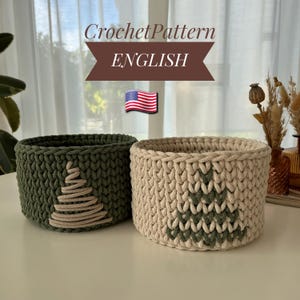 May include: Two handmade crochet baskets. One is olive green with a beige Christmas tree design, the other is beige with a green tree. The text "Crochet Pattern ENGLISH" is at the top, with an American flag.