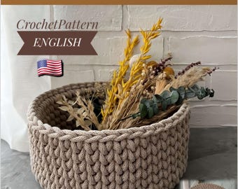 May include: A beige, crocheted basket filled with dried flowers and foliage. The basket has a thick, textured weave and a round shape. The image includes text that says "Crochet Pattern Basket" and "ENGLISH". A bonus crochet pattern for the basket lid is also included.
