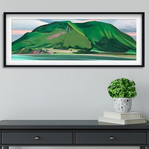 May include: A framed landscape painting of a green mountain with a pink sky and a blue body of water in the foreground.