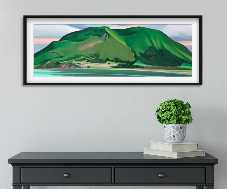 May include: A framed landscape painting of a green mountain with a pink sky and a blue body of water in the foreground.