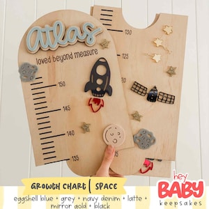 May include: A wooden growth chart featuring space-themed decorations including a rocket, a satellite, stars, and a moon. The chart displays the name Atlas, the text loved beyond measure, and measurement markings ranging from 130 to 150 centimeters.