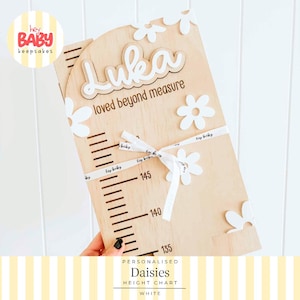 May include: A light-colored wooden height chart featuring the name Luka in white script, the text loved beyond measure, and white daisy cutouts. The board includes black measurement markings from 135 to 145 and is tied with a white ribbon.