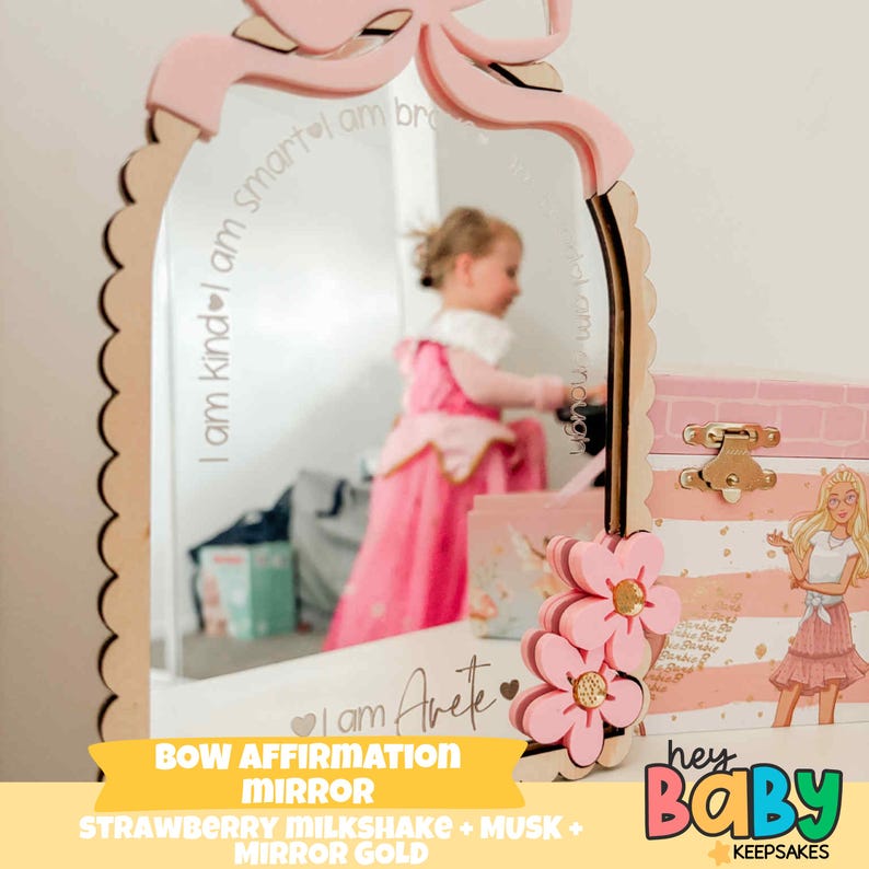 May include: A pink bow-shaped affirmation mirror with a scalloped edge. The mirror has the text "I am kind, I am smart" and "I am Arete". The mirror is decorated with pink flowers and the text "BOW AFFIRMATION MIRROR".