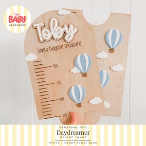 Peut inclure: Une toise en bois portant le prénom Toby et l'inscription loved beyond measure. Le design comprend des découpes de montgolfières bleu clair et blanches, des nuages blancs et une échelle verticale graduée de 135 à 150 en unités métriques.