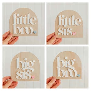 Op de afbeelding: Vier houten borden met gewelfde toppen, elk met witte 3D-letters. De borden lezen "little bro", "little sis", "big sis" en "big bro". Elk bord heeft een klein hartje of cirkel accent.