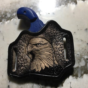 May include: A black leather holster with an eagle design and a blue gun handle.