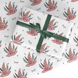 May include: White wrapping paper with a pink witch hat and the text "Basic Witch" repeated throughout. The paper is tied with a green ribbon and the name "freya" is written on the paper.