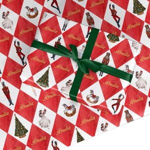 May include: Red and white checked wrapping paper with a Nutcracker theme. The paper features illustrations of a Nutcracker, a ballerina, a rocking horse, and a Christmas tree. The name "Amelia" is repeated throughout the design.