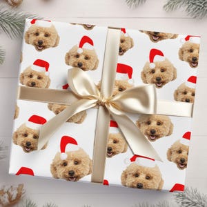 May include: White wrapping paper with a repeating pattern of a dog wearing a Santa hat. The paper is tied with a gold ribbon.