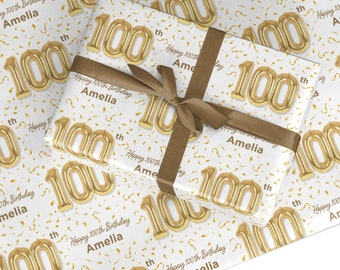 May include: White gift wrap with gold foil confetti and gold foil balloons that spell out "100th". The text "Happy 100th Birthday Amelia" is repeated throughout the wrapping paper.