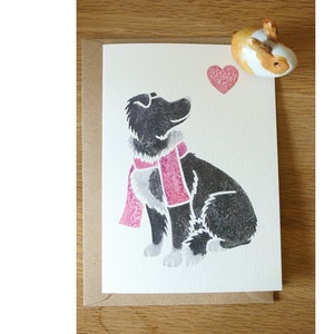 May include: A greeting card featuring a black and white dog wearing a pink scarf and looking up at a pink heart.