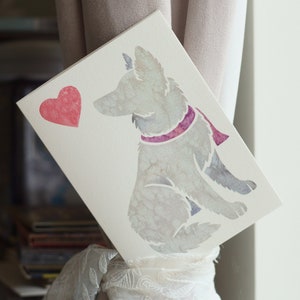 May include: A white card with a watercolor illustration of a dog sitting with a pink scarf. A red heart is in the top left corner of the card.