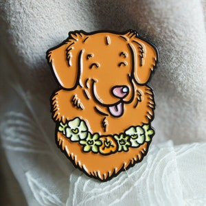 A Toller enamel pin badge shown propped on cream-coloured fabric and white lace.