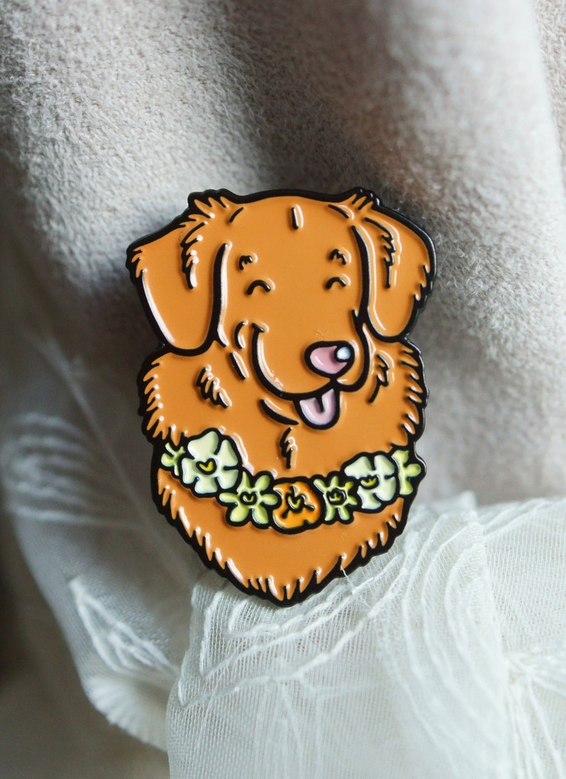 A Toller enamel pin badge shown propped on cream-coloured fabric and white lace.