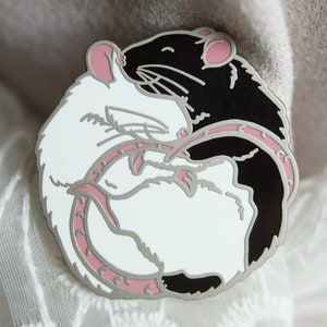 An enamel pin of two rats hugging in a circle, the left is solid white and the right is black and white hooded. The plating colour is satin (matte) nickel.