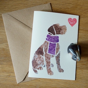 May include: A white card with a brown and white dog wearing a purple scarf. The dog is looking to the right and there is a red heart in the upper right corner of the card.