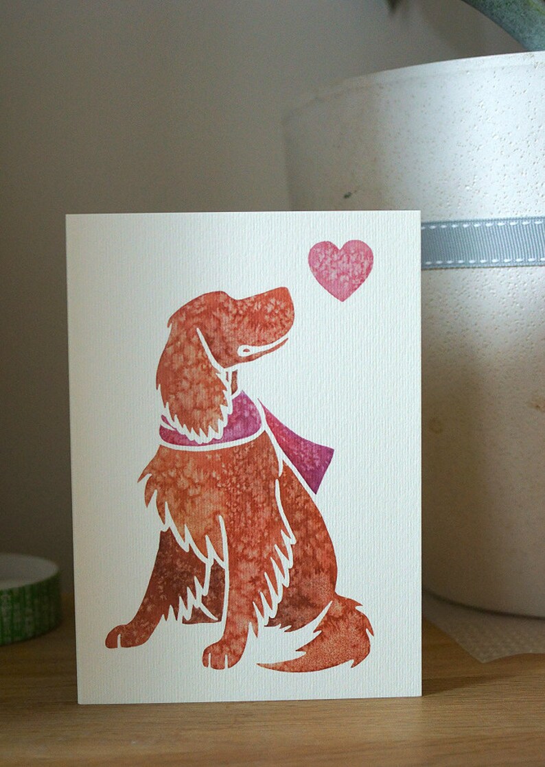 May include: A watercolor illustration of a brown dog with a pink scarf looking up at a pink heart. The dog is sitting on a white card.