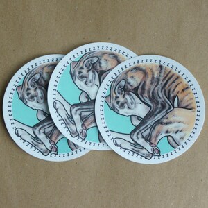 Three sleeping Whippet dog stickers against a brown paper background